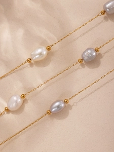 Macro detail of freshwater baroque pearls on a gold chain over textured white sand
