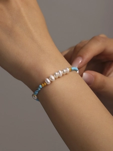 Close-up of handmade pearl bracelet with turquoise beads and gold accents on wrist