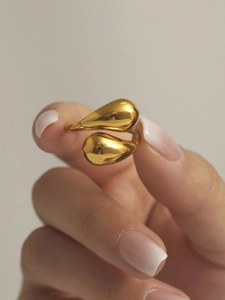 Detail of a polished golden bypass ring featuring a dual teardrop design on a finger