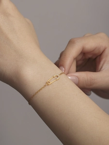 Macro view of gold chain bracelet featuring a safety pin charm with zircon crystals