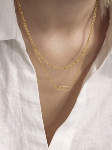 Close-up of a double-layer gold safety pin necklace with sparkling zircons on a model