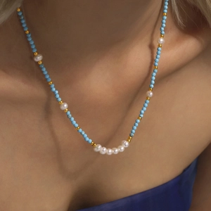 Handmade necklace with turquoise beads, white pearls and gold accents on a model