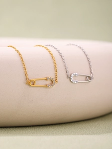 Detail of gold and silver safety pin necklaces with cubic zirconia on a minimalist display