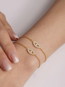 Macro detail of gold layering bracelets featuring a sparkling cubic zirconia evil eye pendant