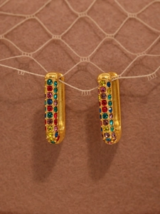 Detail view of gold rectangle earrings with colorful cubic zirconia on warm texture