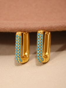 Macro shot of U-shaped gold earrings with turquoise bead inlay on a textured backdrop