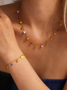 Close-up of gold necklace and bracelet set with colorful enamel heart pendants on a model