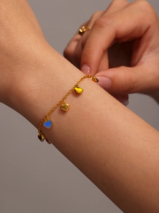 Detail view of a gold chain bracelet with blue, yellow and gold heart-shaped charms