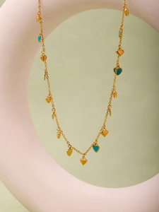 Detail of gold heart necklace featuring teal enamel pendants on a light green background