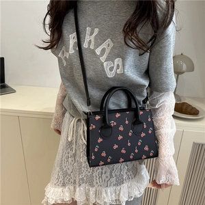 Chic black crossbody bag with cherry print and top handle shown on a female model