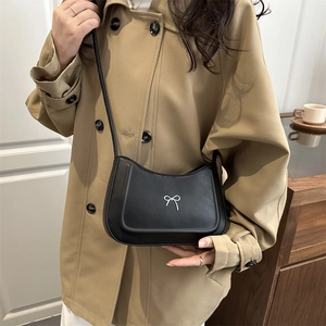 Chic black half-moon shoulder bag with silver bow buckle worn on khaki trench coat