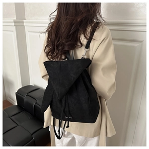 Rear view of a model wearing a unique black suede backpack with triangle flap and ear detail