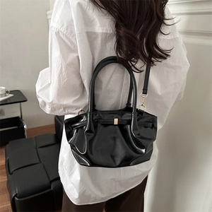 Chic black glossy bucket bag with ruched design and gold buckle shown on a shoulder