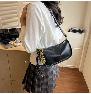 Detail view of black crescent underarm bag with gold tennis racket charm on shoulder