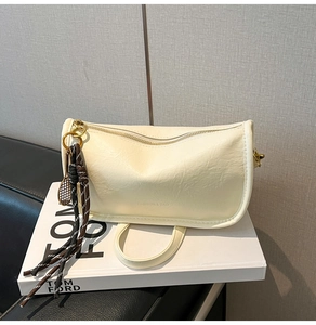Détail du sac bandoulière plissé crème avec breloque raquette de tennis sur un livre