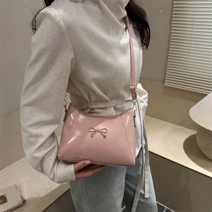 Pink glossy crossbody bag with golden bow metallic buckle shown on model