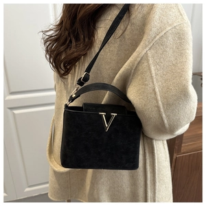 Detail van zwarte matte crossbodytas met gouden V-metaalbeslag op een beige jasje