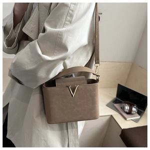 Detail of tan structured handbag with gold V metal logo on beige trench coat outfit