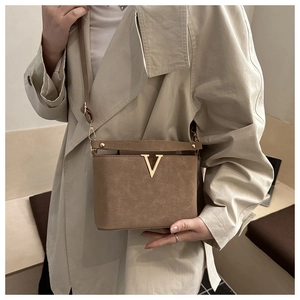 Detail van bruine crossbodytas met goudkleurig V-logo en korrelige kunstlederen textuur