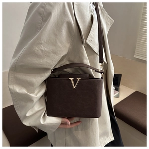 Detail van donkerbruine crossbodytas met gouden V-gesp gedragen op beige trenchcoat
