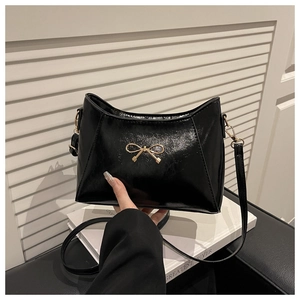 Detail of black patent leather shoulder bag with gold bow clasp and shoulder strap