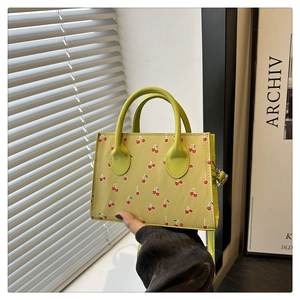 Dettaglio di una piccola borsa a mano verde chiaro con stampa a ciliegie e manici tondi