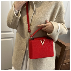 Detail view of red leopard-textured leather bag with metallic gold V-shaped buckle