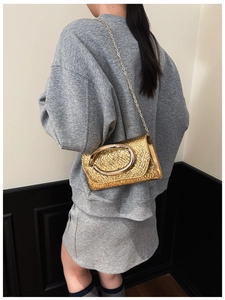 Close-up of golden clutch bag with woven texture and large oval buckle on a chain strap