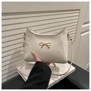 Close-up of textured beige shoulder bag featuring a gold-tone metal bow clasp detail
