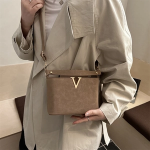 Bruine vintage crossbodytas met gouden V-sluiting gedragen met een beige trenchcoat