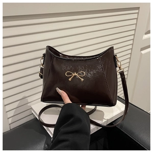 Detail of dark brown patent leather shoulder bag with gold bow ornament and glossy finish
