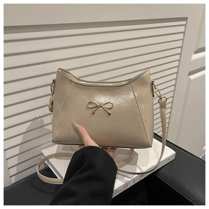Detailed shot of beige glossy shoulder bag featuring an elegant gold bow hardware detail