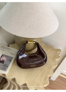Vue détaillée du sac en cuir verni marron foncé avec fermoir doré sur une table en bois