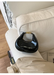 Détail du sac hobo en cuir verni noir avec boucle dorée sur un canapé crème