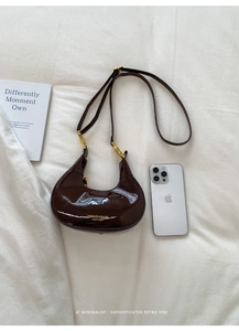 Close-up of glossy brown patent leather crescent bag with golden chain and logo detail