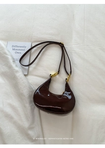 Detail of a brown glossy crescent bag with gold hardware on a white linen backdrop