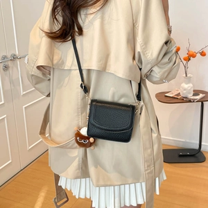 Minimalist black pebbled leather underarm bag with a cute brown monster plush charm