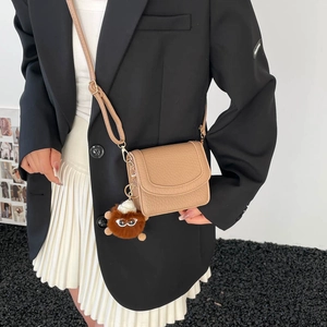 Brown leather crossbody bag with faux fur charm accessory shown on minimalist model