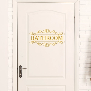 Détail d'un autocollant de porte doré Bathroom avec bordure florale sur porte blanche