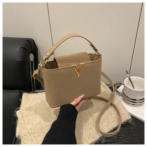 Detail of khaki leather bucket bag with gold V-buckle on a cozy knitted blanket