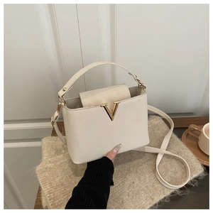 Detail of a cream trapezoid leather handbag with a gold V-shaped metal clasp buckle