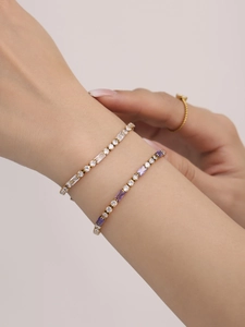 Close-up of stacked gold tennis bracelets with purple and clear zircon stones on wrist