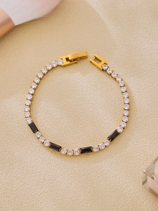 Detail of gold-plated tennis bracelet with black and clear stones on beige background