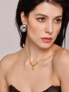 Details von silbernen Halbkugel-Ohrsteckern und goldener Halskette an einem Model