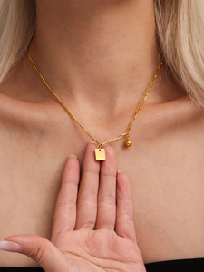 Dettaglio del ciondolo quadrato dorato con incisione Good Luck su una collana a catena