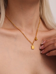 Dettaglio della collana dorata con ciondolo a piastra quadrata e scritta Good Luck