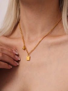 Dettaglio del ciondolo Good Luck dorato e collana a catena asimmetrica indossata