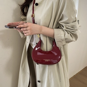 Glossy burgundy crescent shoulder bag with chain strap shown on beige trench coat