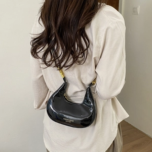 Glossy black crescent shoulder bag with gold hardware worn by model from behind