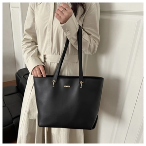Close-up of black leather tote bag with metallic logo plate and gold hardware details